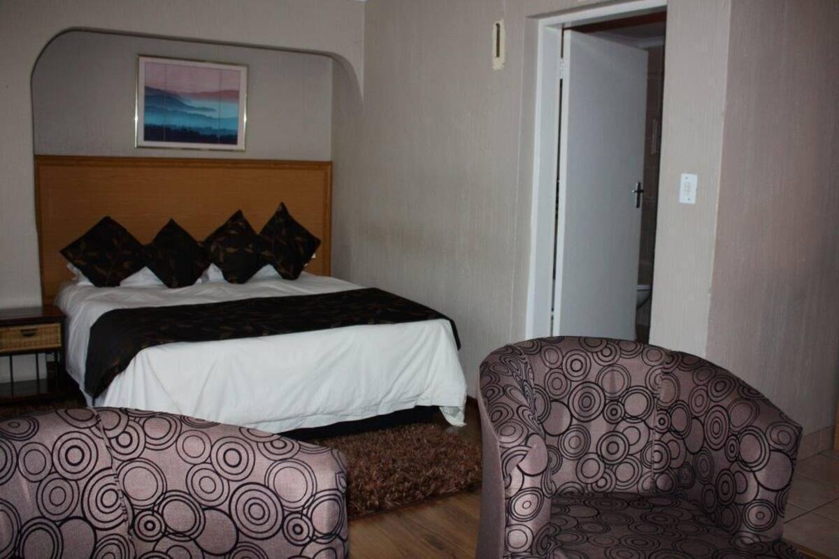 A hotel room with a bed, a headboard, a pillow, a chair, and a door.