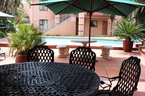 Un patio con una mesa y sillas metálicas redondas, una piscina al fondo y una escalera que lleva a un nivel superior.