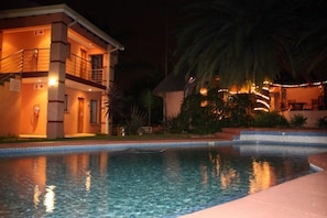 Un hotel con piscina, balcón y una entrada bien iluminada.