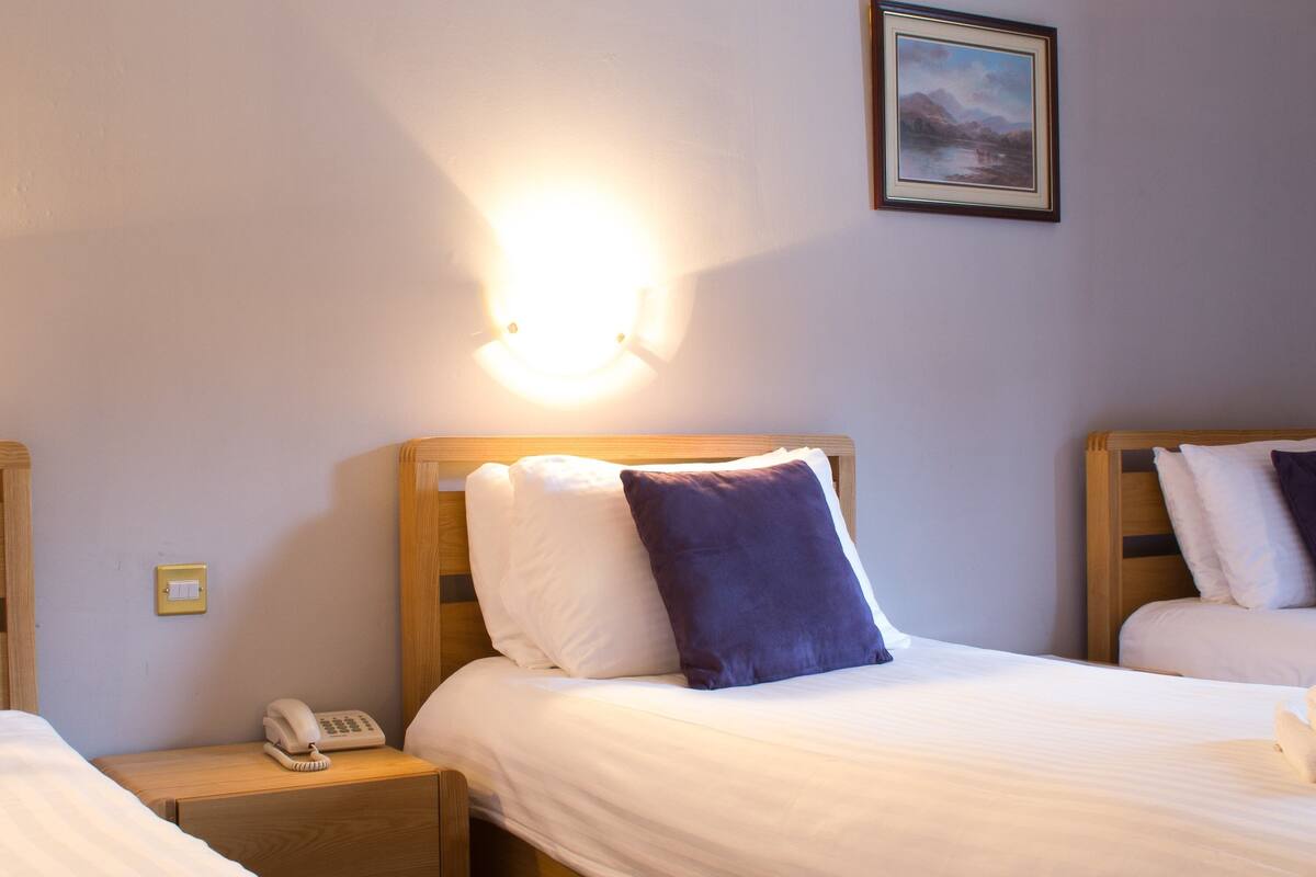 A hotel room with two beds, a bedside table with a phone, and a wall-mounted light fixture.