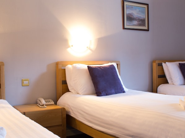 Una habitación de hotel con dos camas, una mesita de noche con teléfono y una lámpara fijada a la pared.