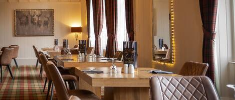 A dining area with a checkered floor, wooden tables, leather chairs, a chandelier, plaid curtains, and a mirror with lights.