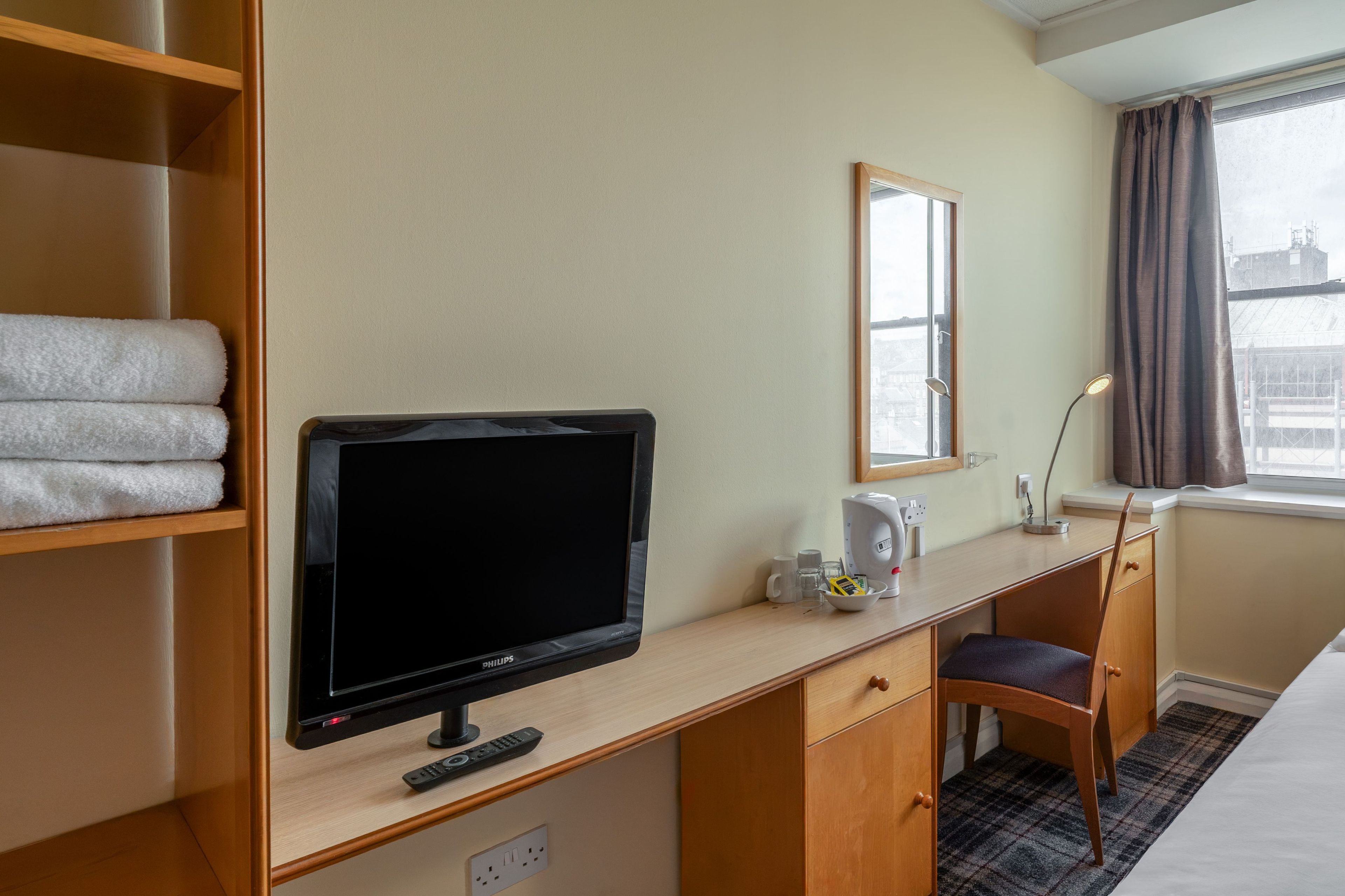 Una habitación de hotel con escritorio, televisión, espejo, ventana con cortinas y cama.