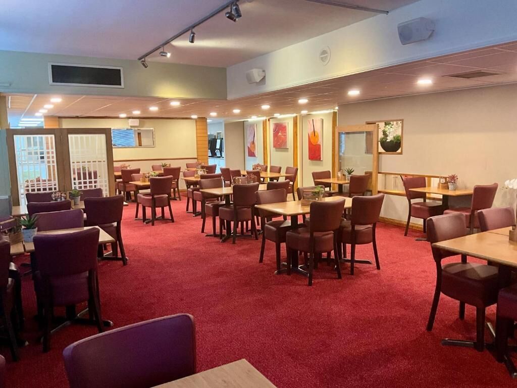 A spacious dining area with multiple tables and chairs, a red carpet floor, and artwork on the walls.