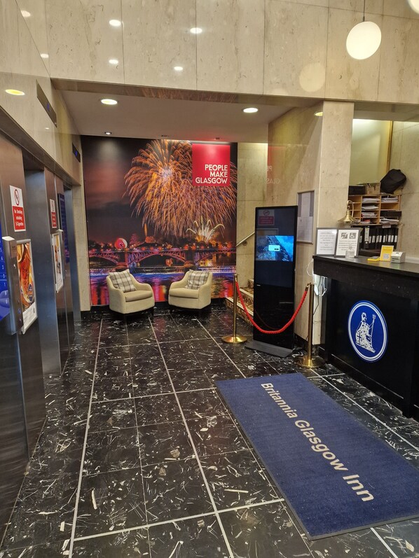 A lobby with a large firework display poster, two armchairs, a reception desk, and a blue carpet with "Glasgow Inn" text. - Britannia Inn Glasgow (Glasgow)