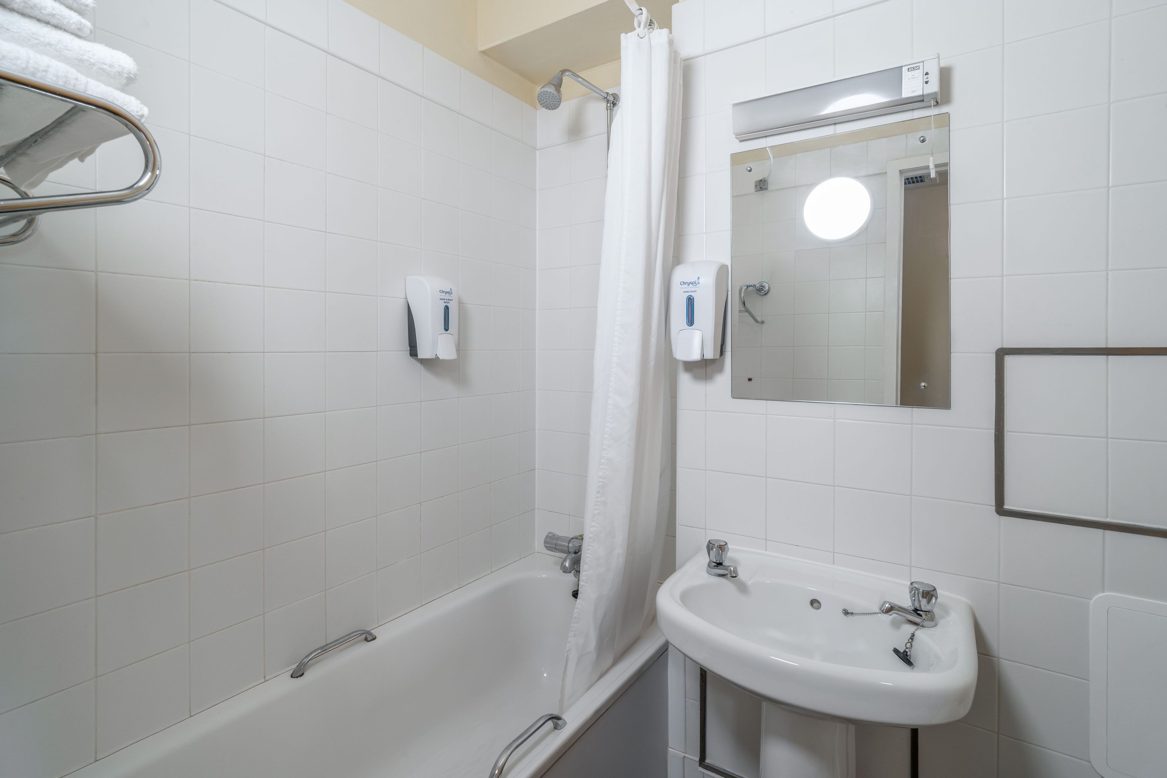 A bathroom with a bathtub, a sink, a mirror, and a towel rack.