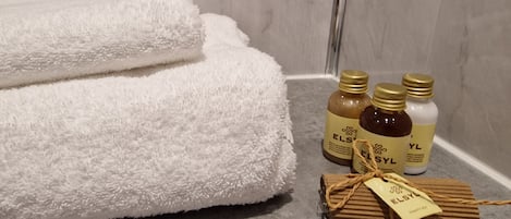A bathroom with a white towel, two bottles of ELSYL body care products, and a vanilla kit on a marble countertop.