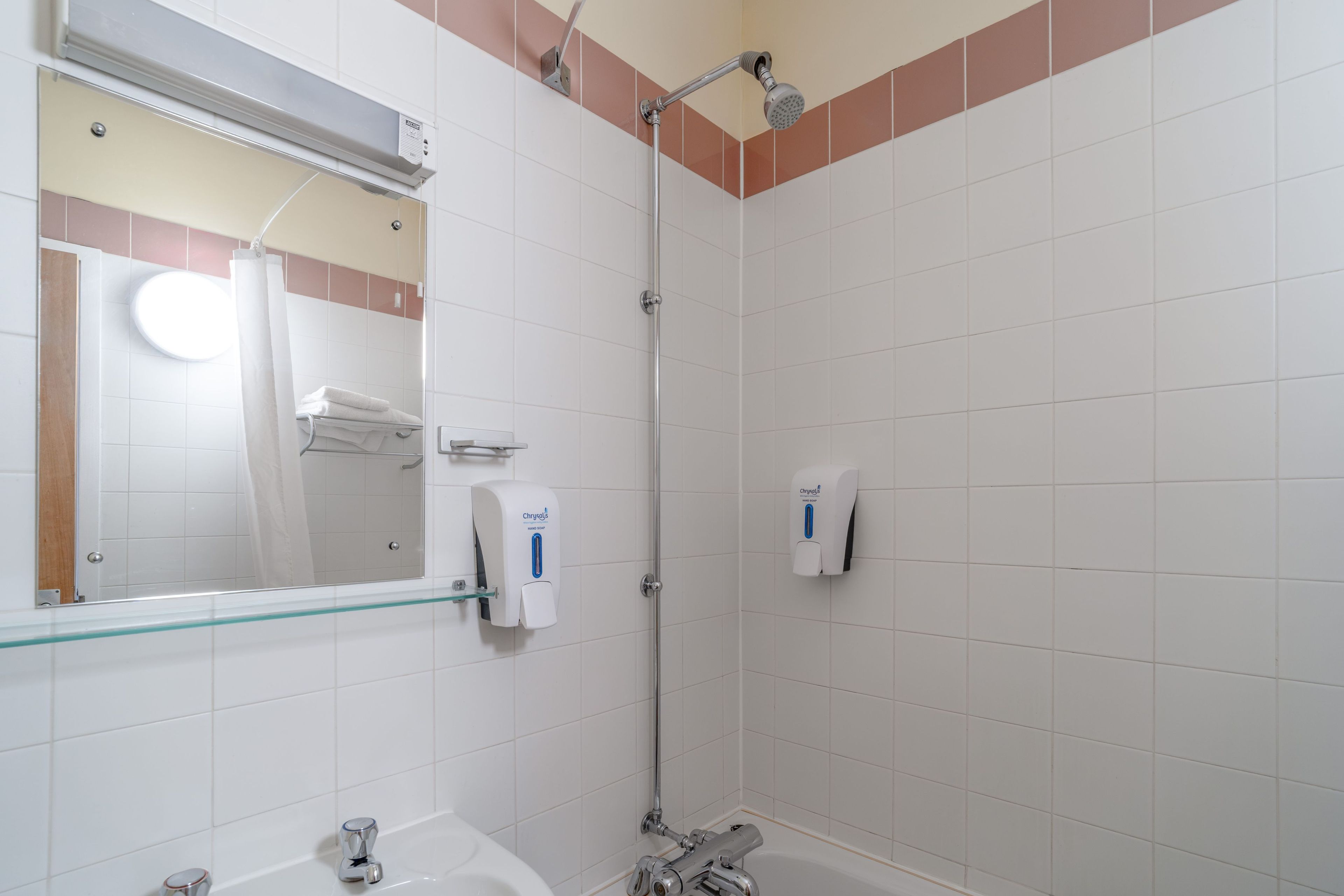 A bathroom with a glass shower enclosure, a hand soap dispenser, and a mirror.