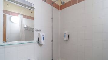 A bathroom with a glass shower enclosure, a hand soap dispenser, and a mirror.
