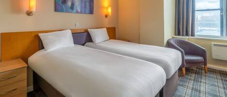 Une chambre d’hôtel avec deux lits, une chaise, un tableau au mur et une fenêtre avec des rideaux.