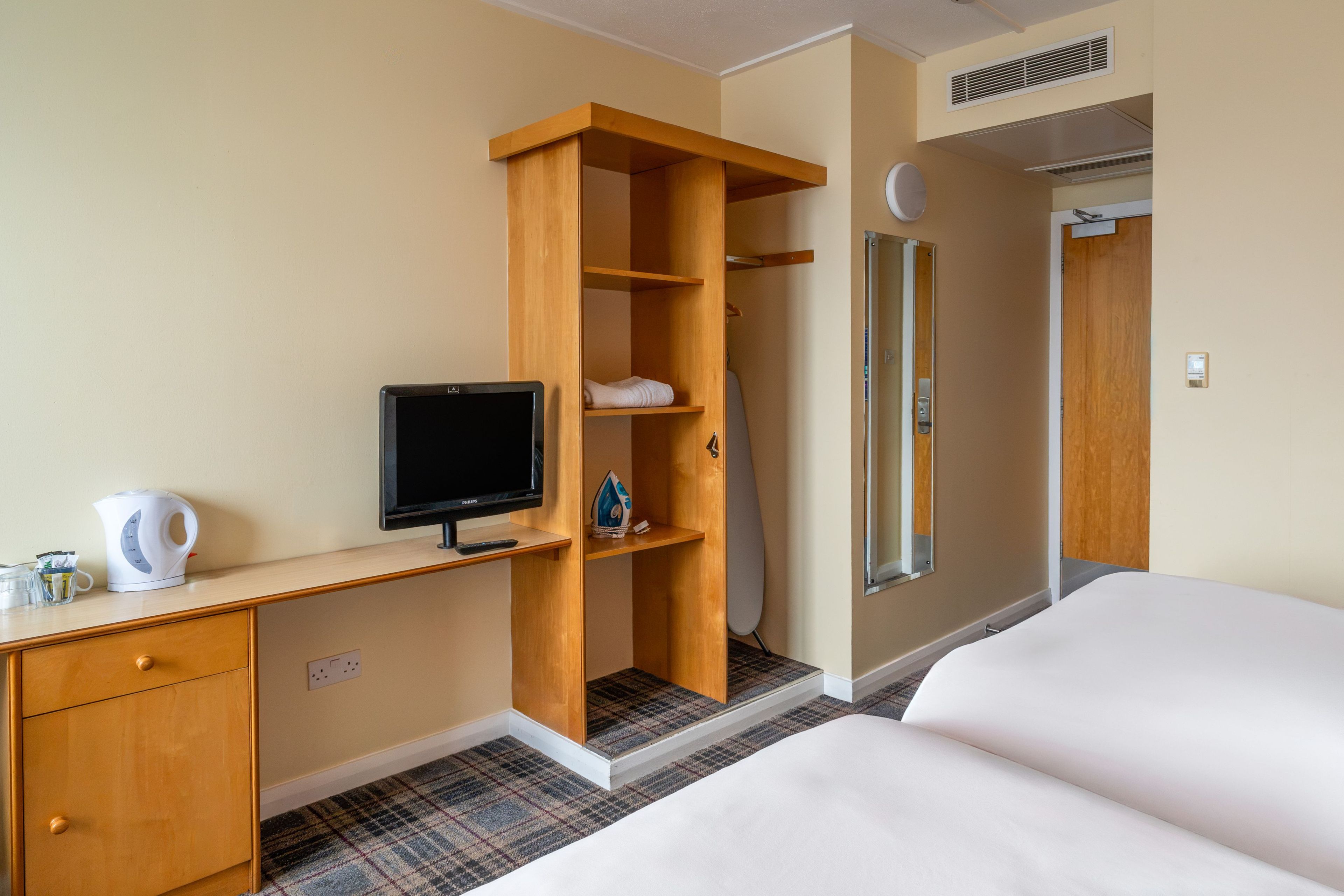 A hotel room with a bed, a desk with a television, a wardrobe, and a bathroom.