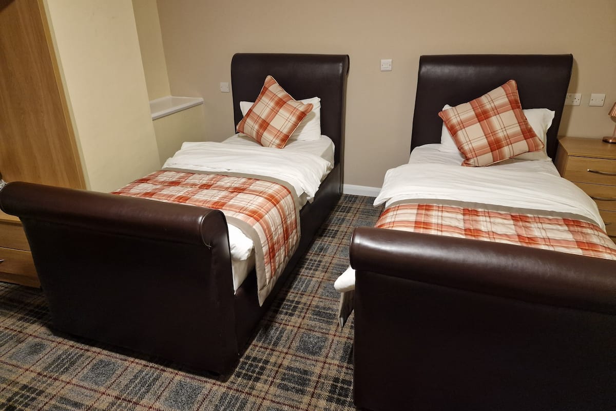 Two twin beds with brown headboards and plaid bedding, a wooden nightstand, and a patterned carpet.