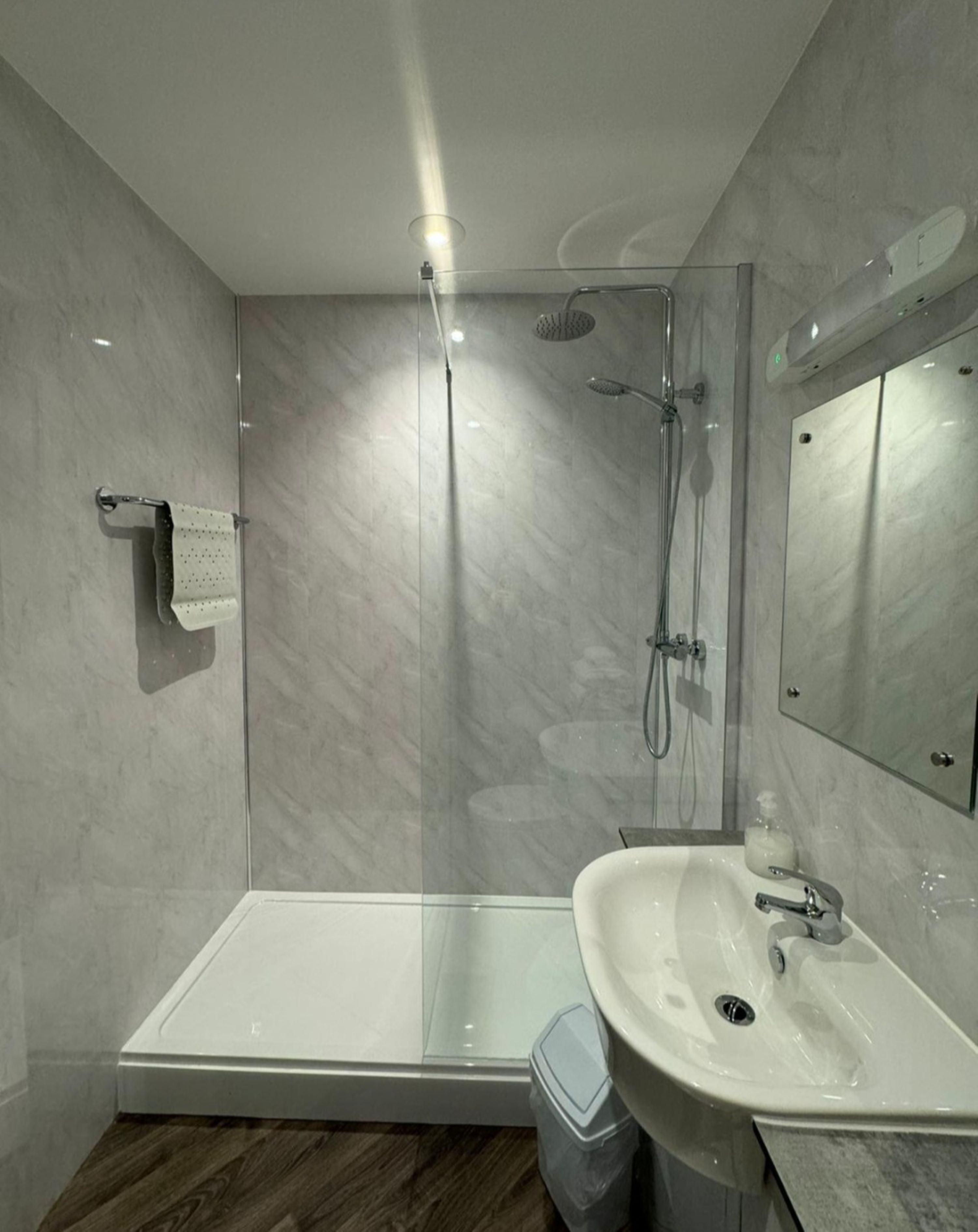 A modern bathroom with a glass-enclosed shower, a white sink, and a mirror above it.