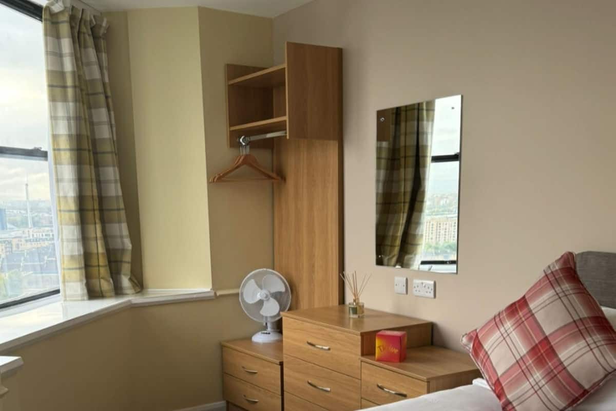 A hotel room with a bed, a dresser, a mirror, and a window with curtains.