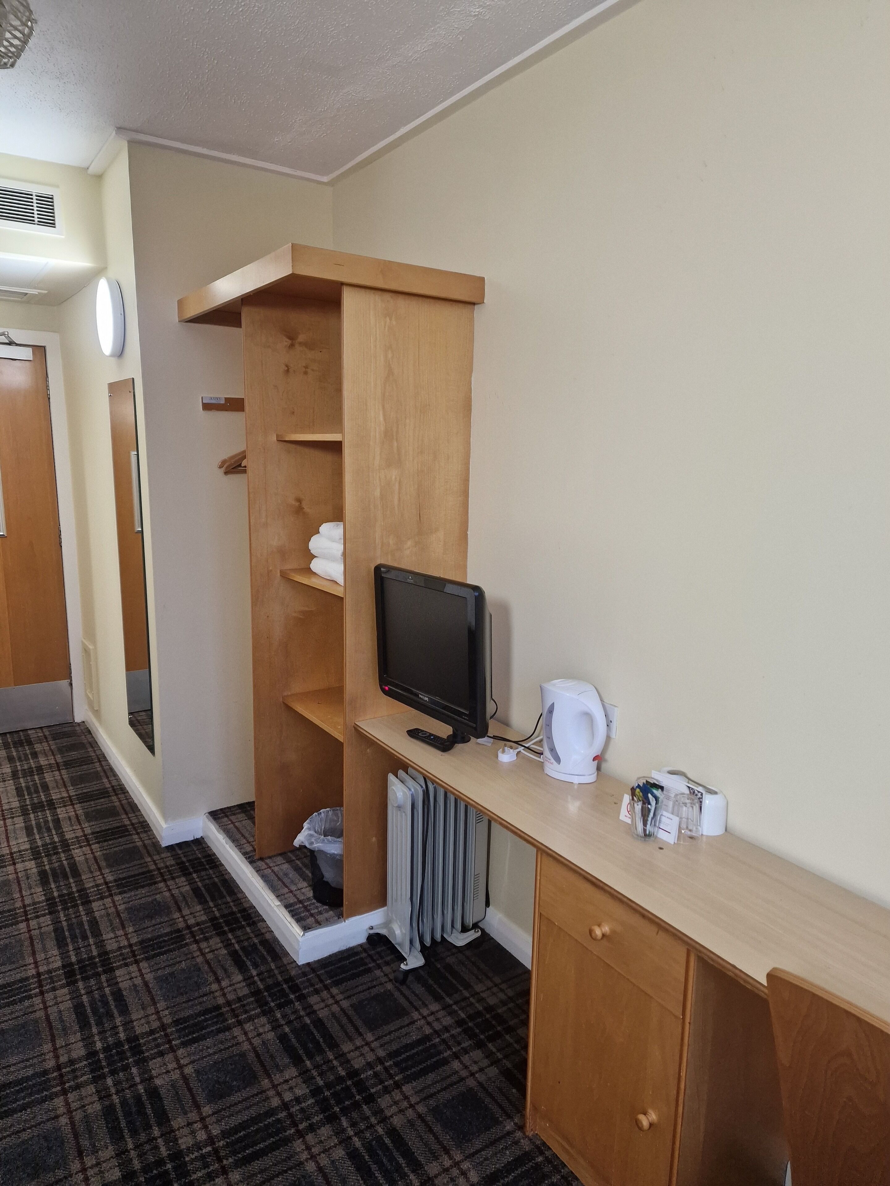 Ein Hotelzimmer mit einem Holztisch, einem Fernseher, einem Wasserkocher und einer Heizung.
