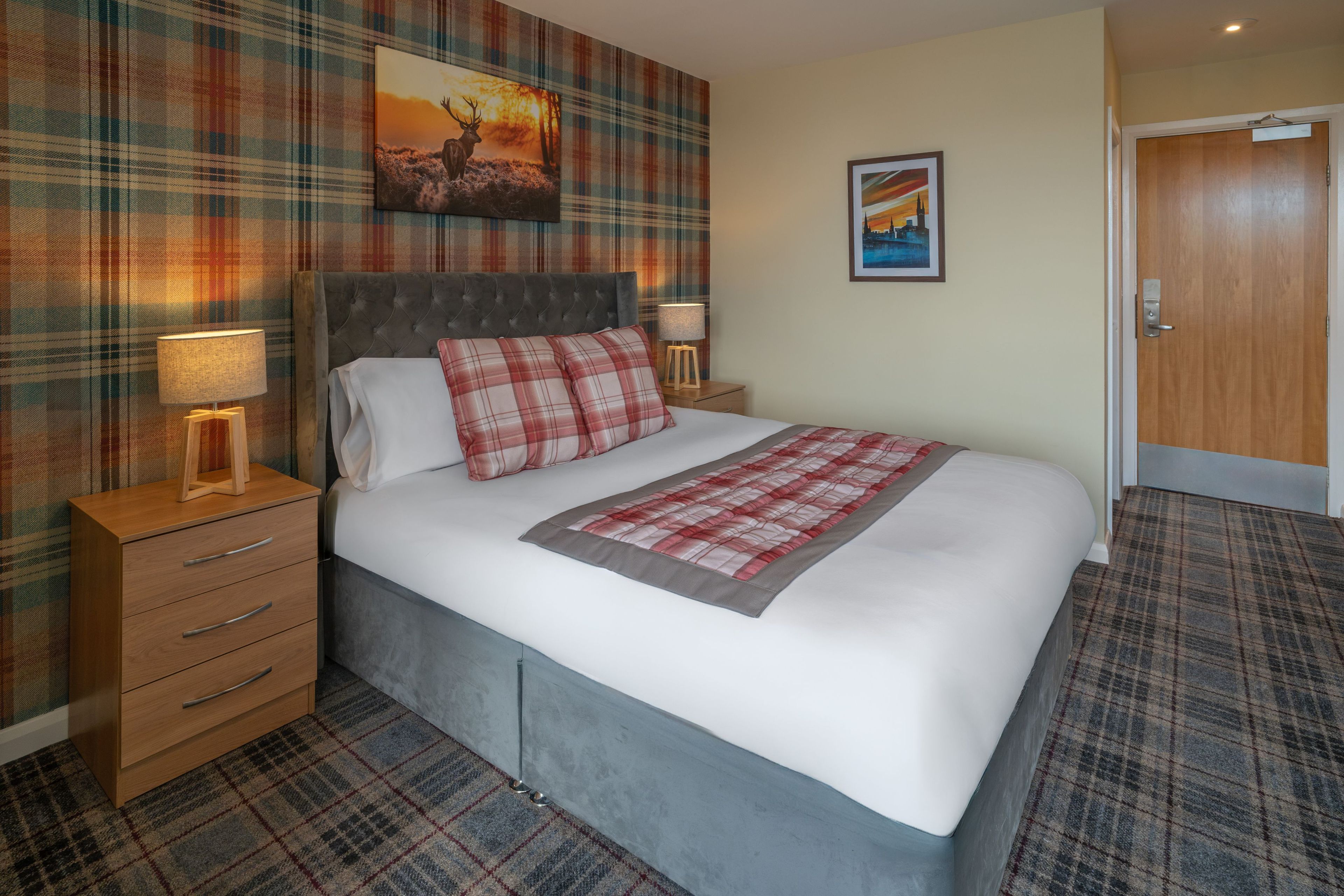 Ein Hotelzimmer mit Bett, Nachttisch, Lampe, Kommode und Tür.