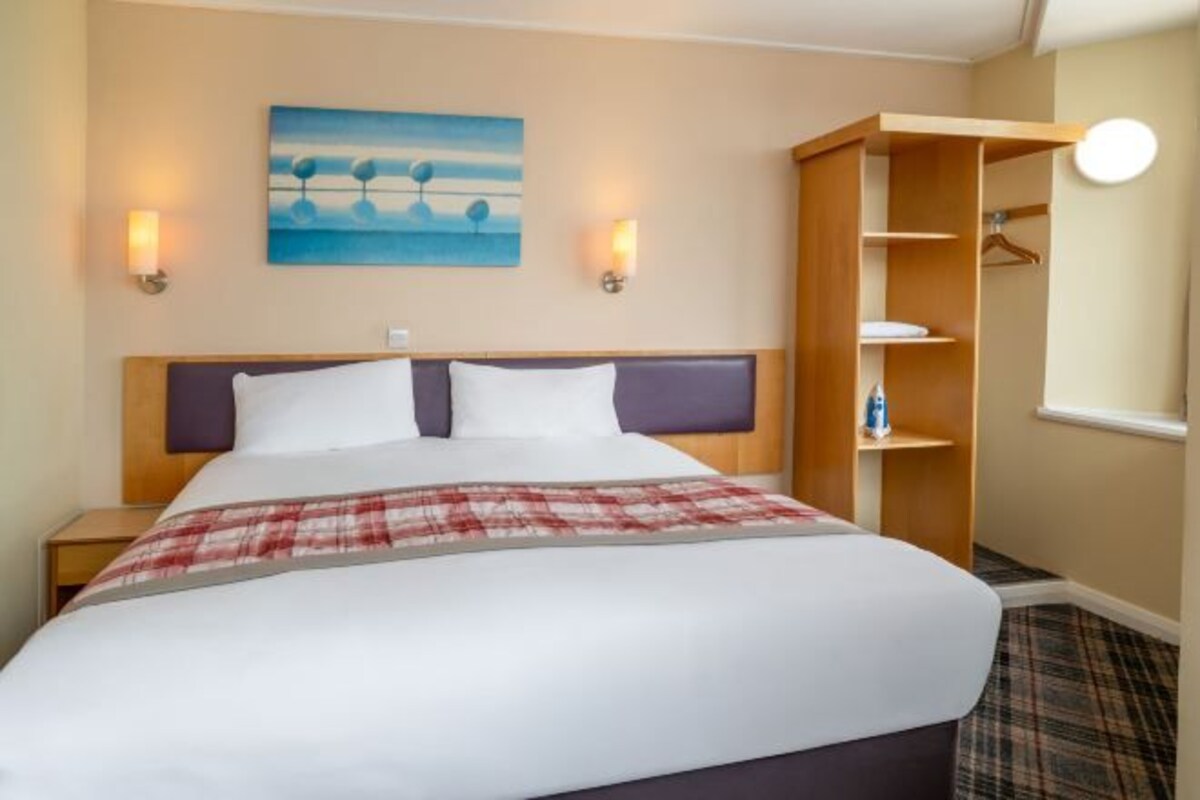 A hotel room with a bed, a nightstand, a wardrobe, and a painting on the wall.