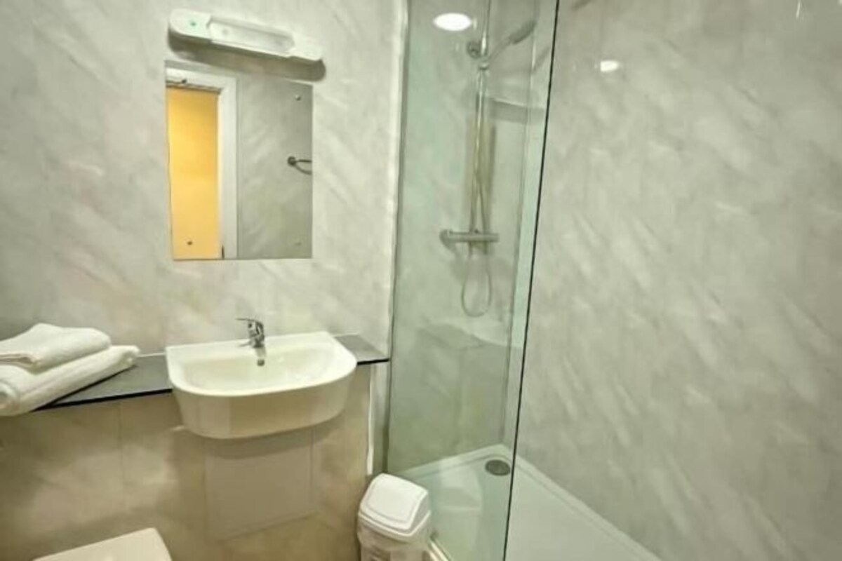 A modern bathroom with a glass-enclosed shower, a white sink, and a mirror above it.