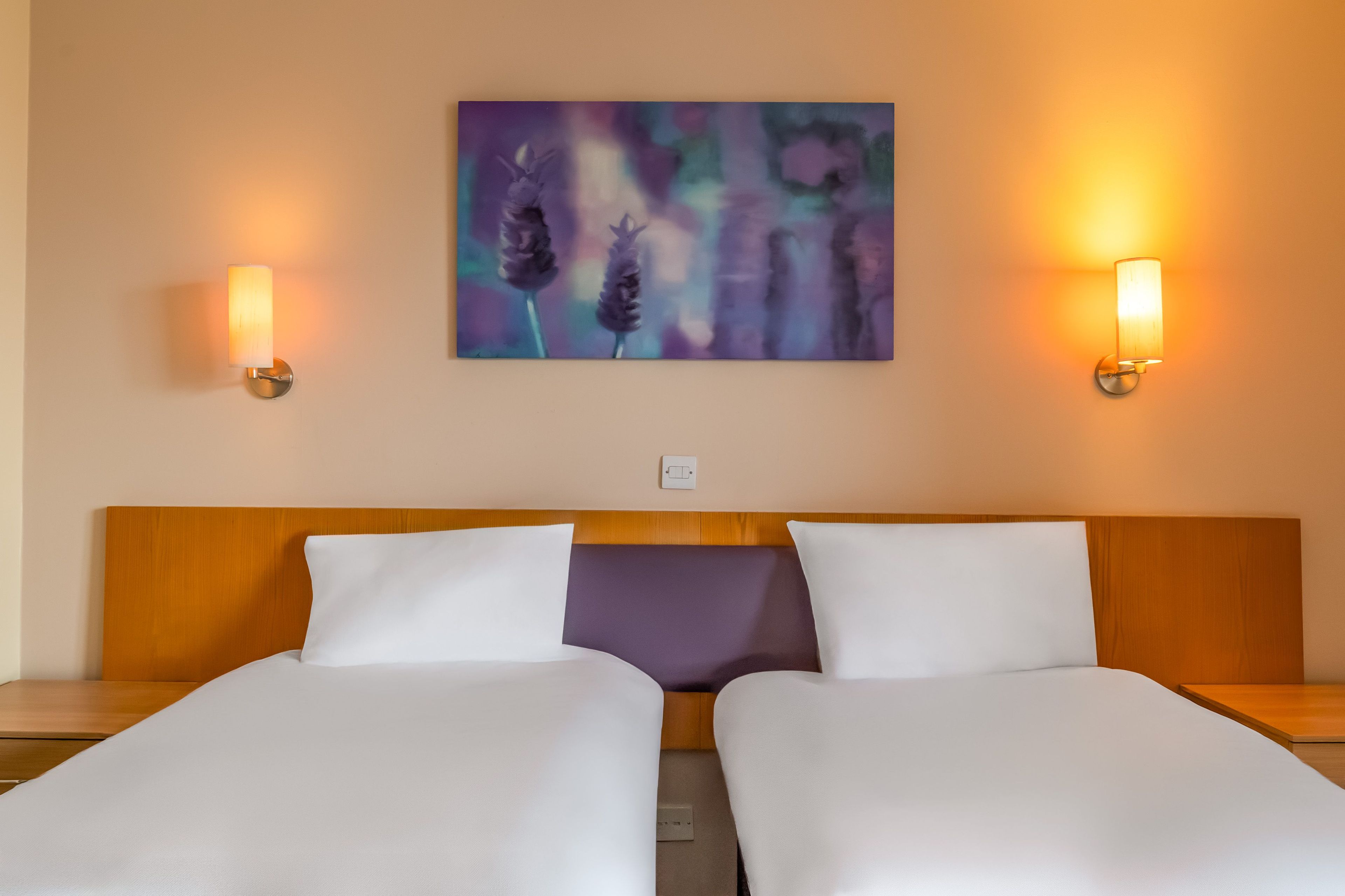 Ein Hotelzimmer mit zwei Betten, einem Holzkopfteil und einem an der Wand hängenden Gemälde.