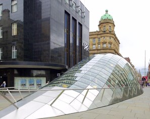 A modern glass structure with a reflective surface, adjacent to a historic building with a green dome. - Britannia Inn Glasgow (Glasgow)