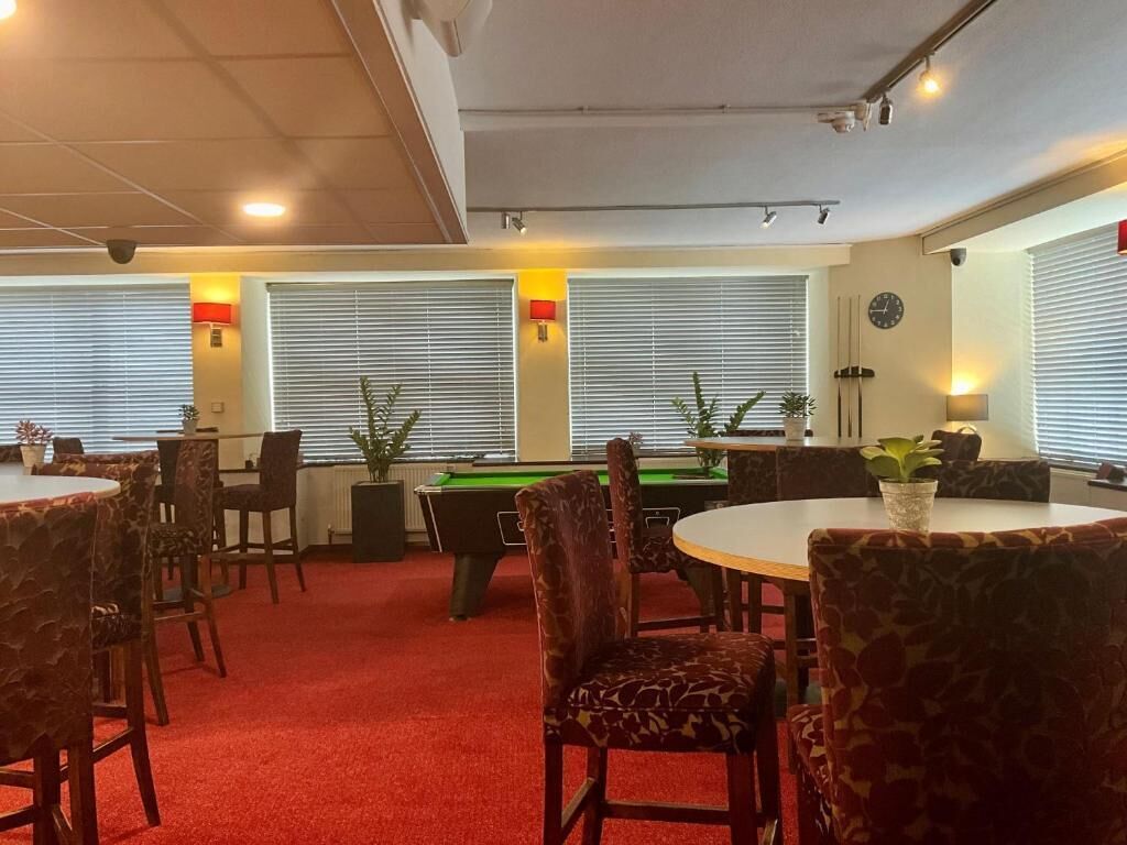 A room with a pool table, red carpet, and multiple seating areas with patterned chairs.