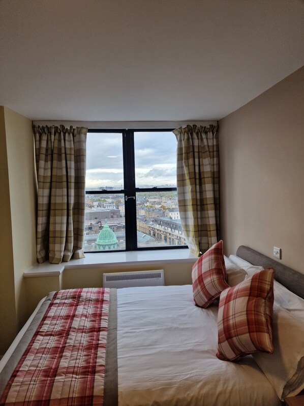 A hotel room with a large window, a bed with a plaid bedspread, and two pillows. - Britannia Inn Glasgow (Glasgow)