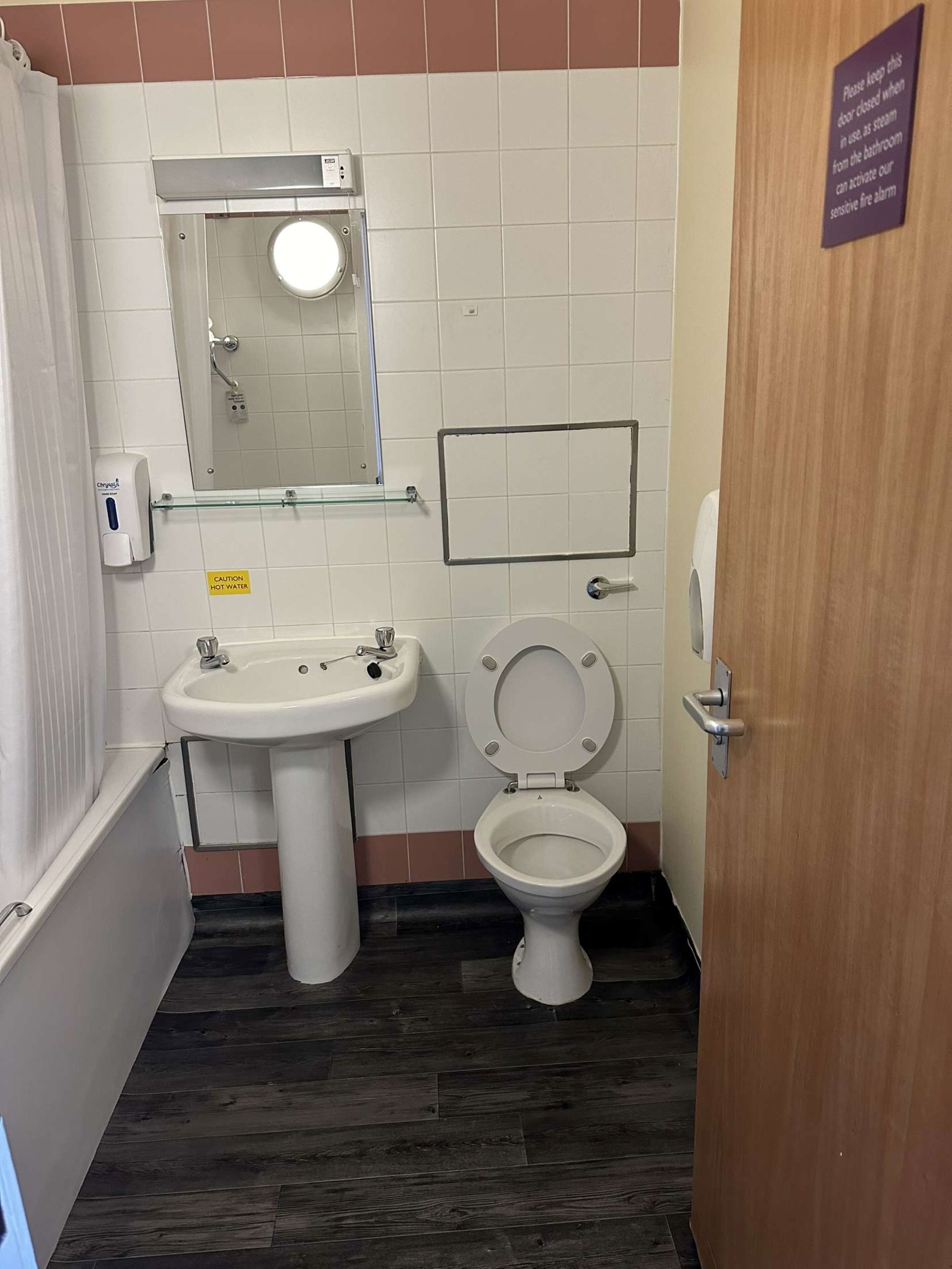 A bathroom with a white sink, a toilet, a mirror, and a caution sign for hot water.