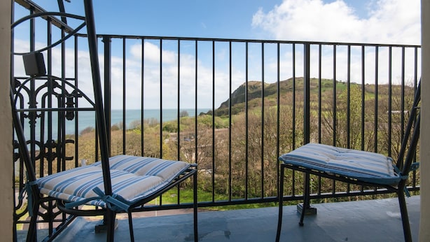 Un balcón con dos sillones con cojines a rayas que dan a una vista panorámica de colinas y el mar.