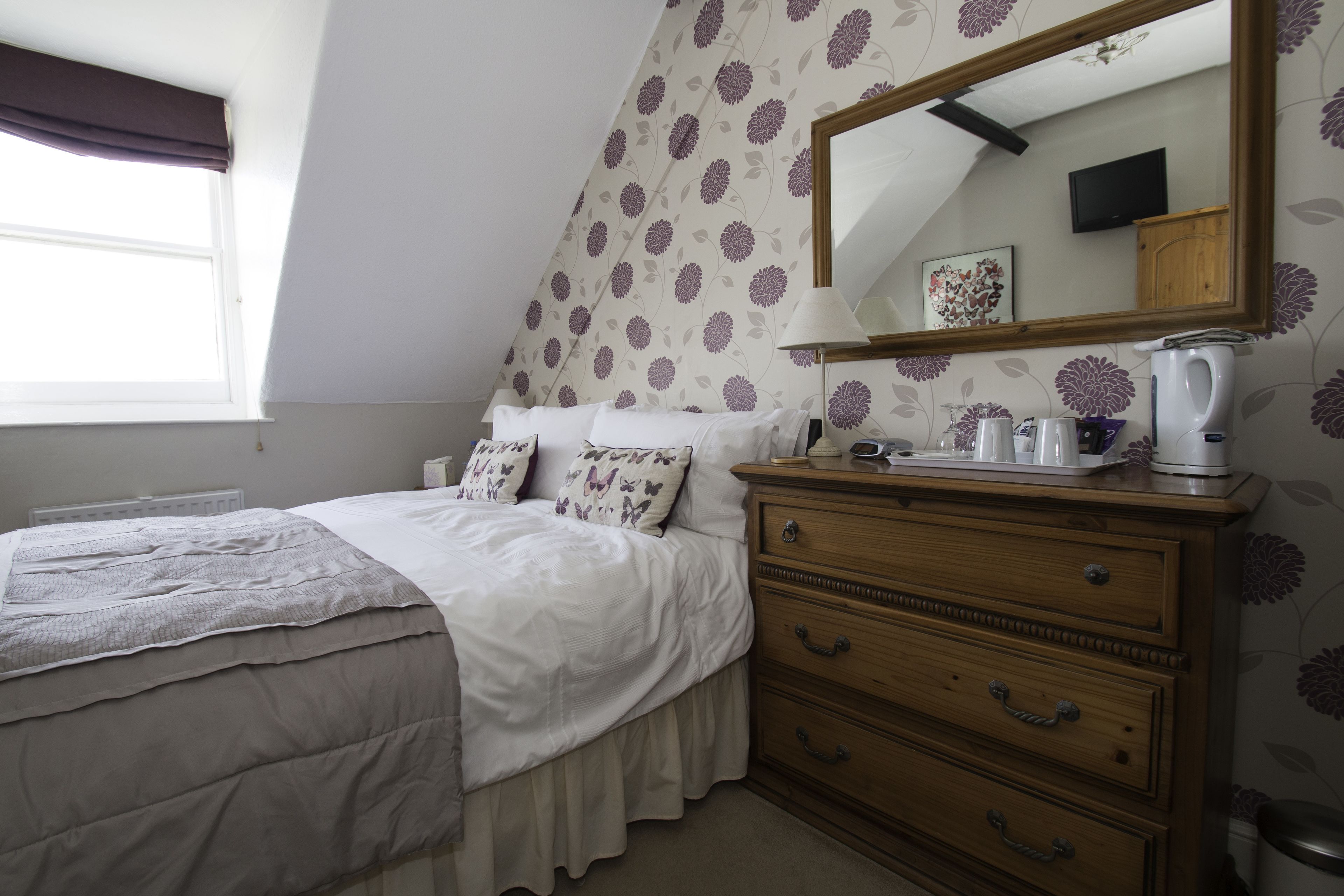 A bedroom with a bed, dresser, mirror, and a window.
