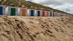 Una hilera de cabañas portátiles de colores sobre una pendiente arenosa, con una colina cubierta de hierba al fondo.