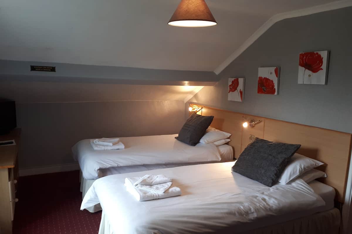 A hotel room with two beds, each with white linens and towels. There is a ceiling lamp, a bedside table, and a wall-mounted light.