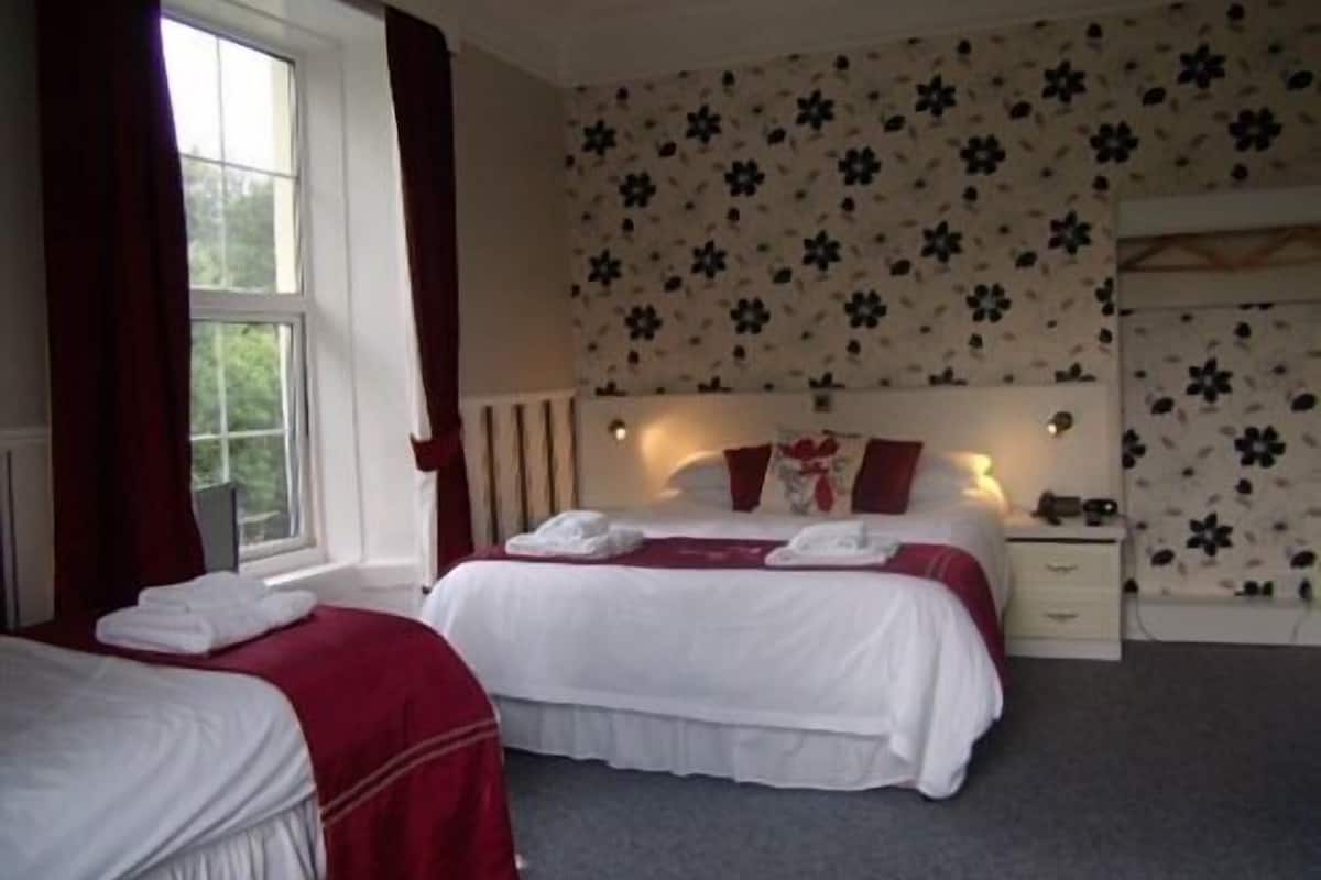 A double room with two beds, a window with curtains, a nightstand with a lamp, and floral wallpaper.