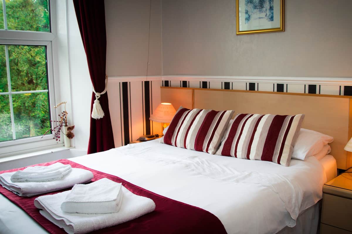 A neatly made bed with striped pillows, a red throw blanket, and folded towels on a white bedspread. A lamp is on the nightstand beside the bed.
