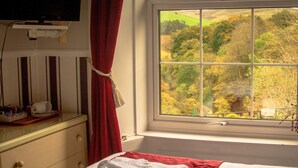 A hotel room with a bed, a window with a view of a forest, a red towel on the bed, and a small table with toiletries. - George Borrow Hotel (Aberystwyth)
