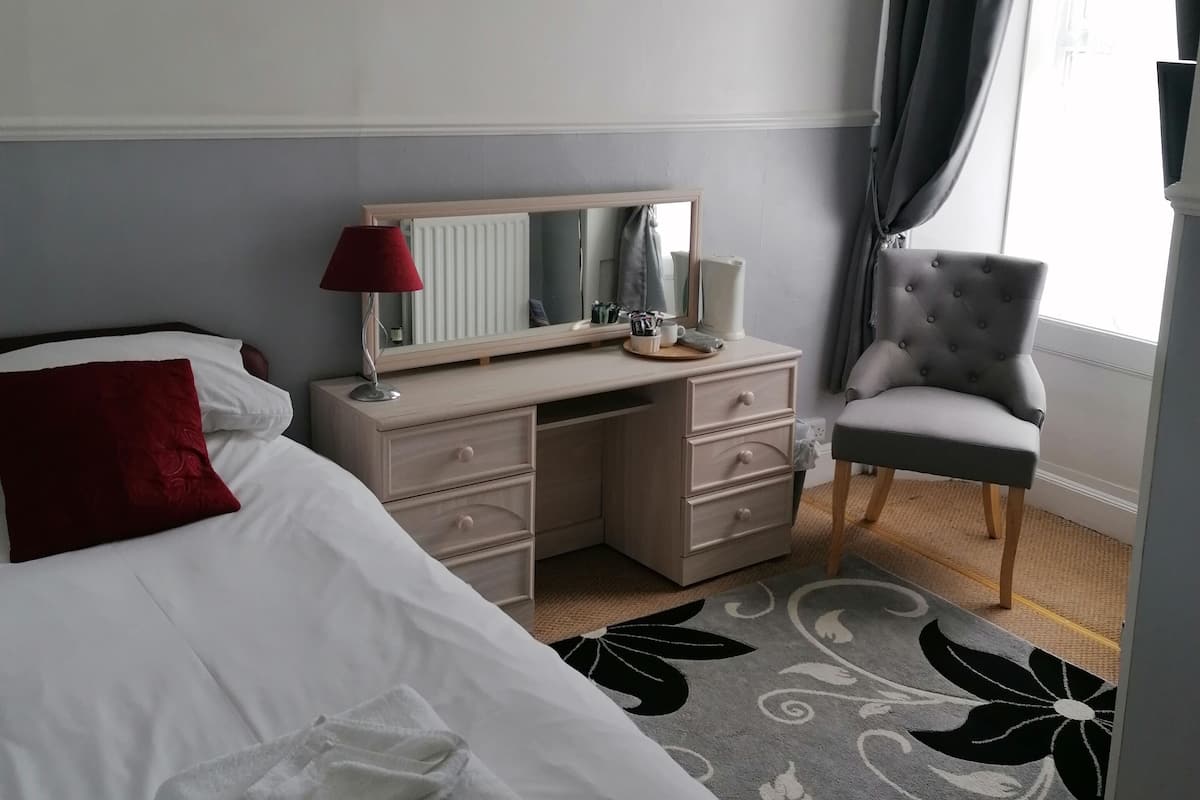 A hotel room with a bed, a desk, a chair, a dresser, and two framed pictures on the wall.