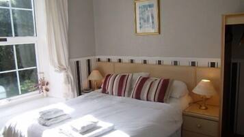 A neatly made bed with white linens and striped pillows, a bedside table with a lamp, and a framed picture on the wall.