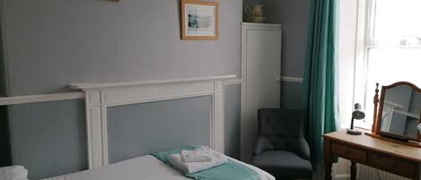 Una habitación de hotel con cama, escritorio con espejo, silla y armario.