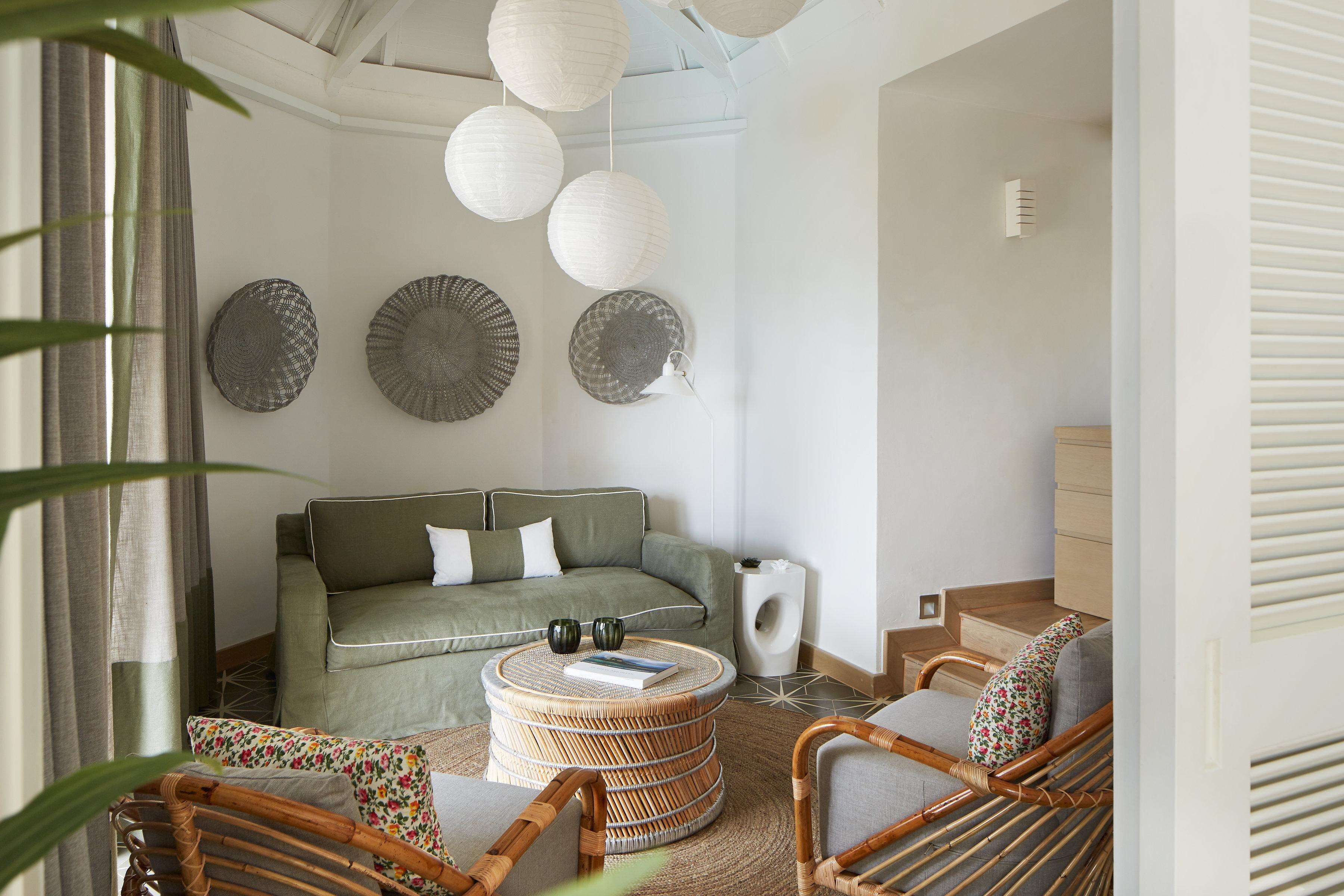 Una sala de estar con un sofá verde, sillas de mimbre, una mesa de centro redonda y platos decorativos en la pared.
