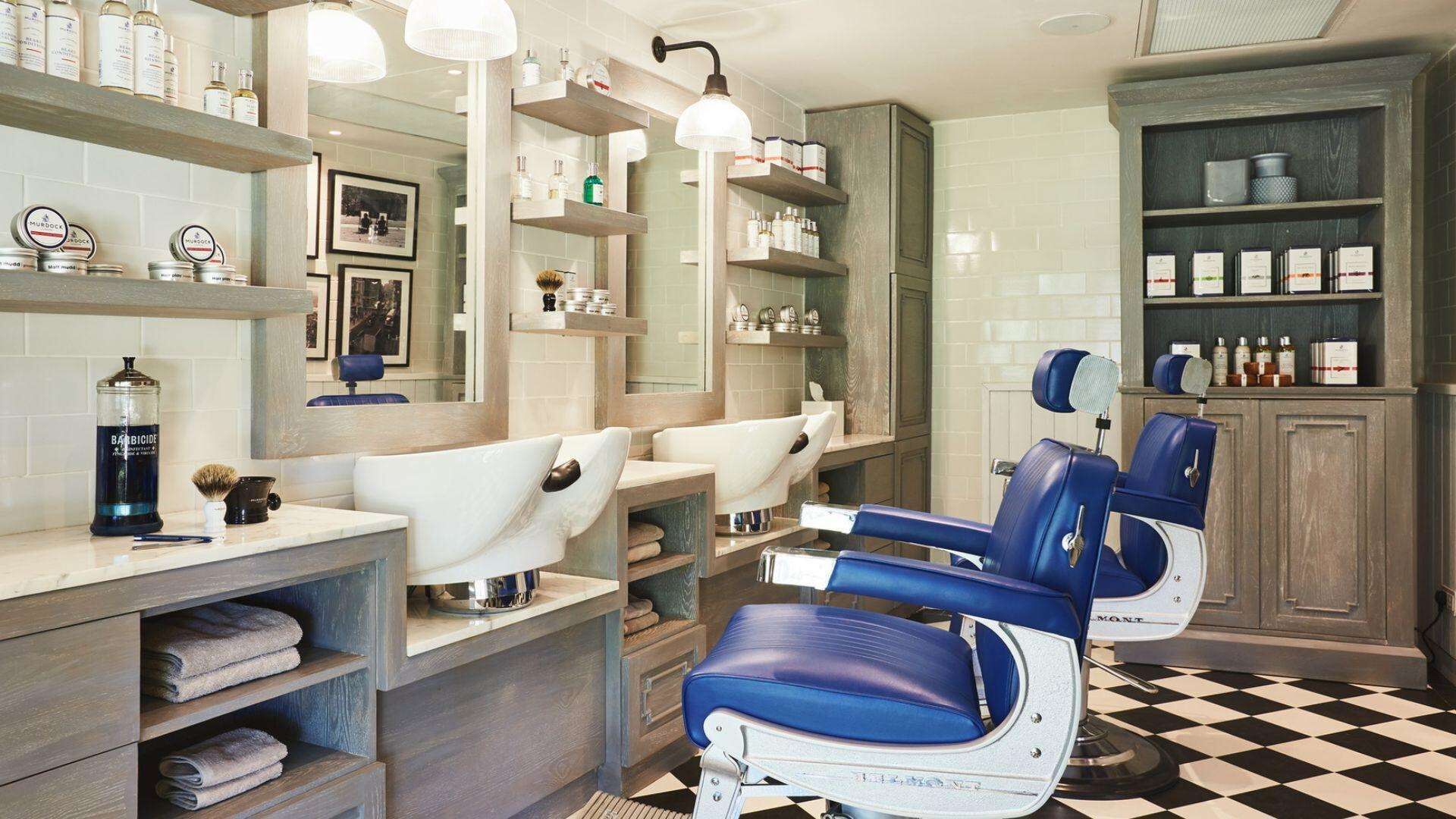 A modern bathroom with two barber chairs, shelves with toiletries, and a checkered floor.