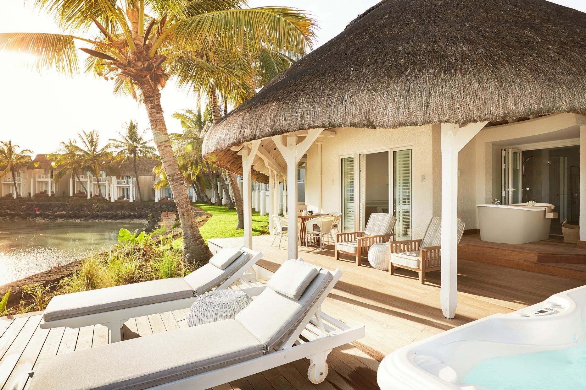 A resort with a pool, lounge chairs, a thatched-roof structure, and a view of the ocean.