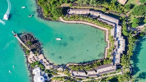 An aerial view of a resort with a large central lagoon, surrounded by palm trees and a fortified structure. - LUX* Grand Gaube (Grand Gaube)