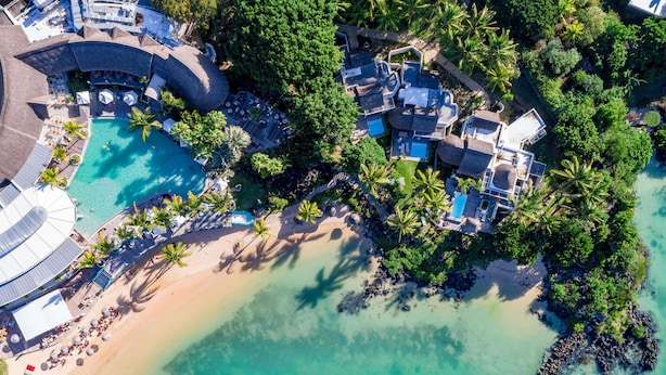 An aerial view of a resort with a large swimming pool, beach area, and multiple guest villas surrounded by lush greenery. - LUX* Grand Gaube (Grand Gaube)