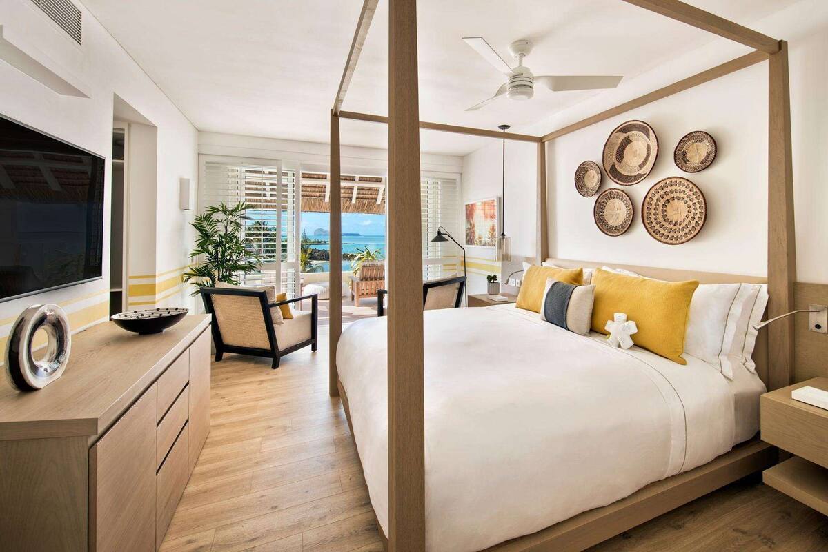 A modern bedroom with a four-poster bed, wooden flooring, and a view of the ocean.