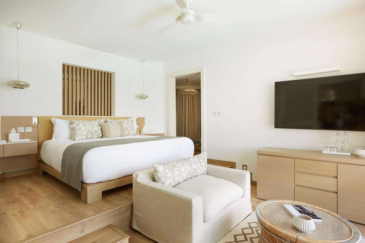 A modern hotel room with a large bed, a sofa, a TV, and a desk.