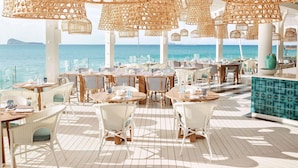 An outdoor dining area with wicker furniture and hanging light fixtures, overlooking the sea. - LUX* Grand Gaube (Grand Gaube)