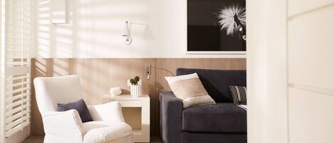A modern living room with a white armchair, a dark sofa, a small side table with a plant, and a wall-mounted lamp.