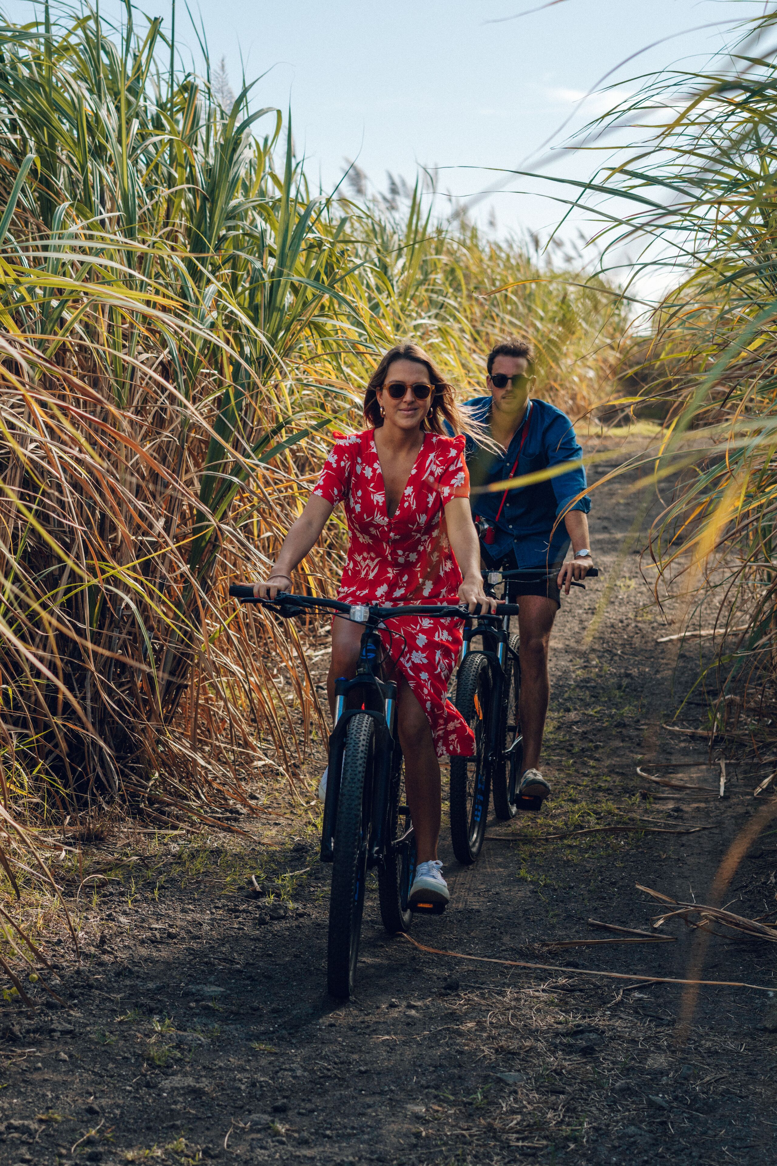 Dos personas montando en bicicleta por un sendero de tierra rodeado de hierba alta.
