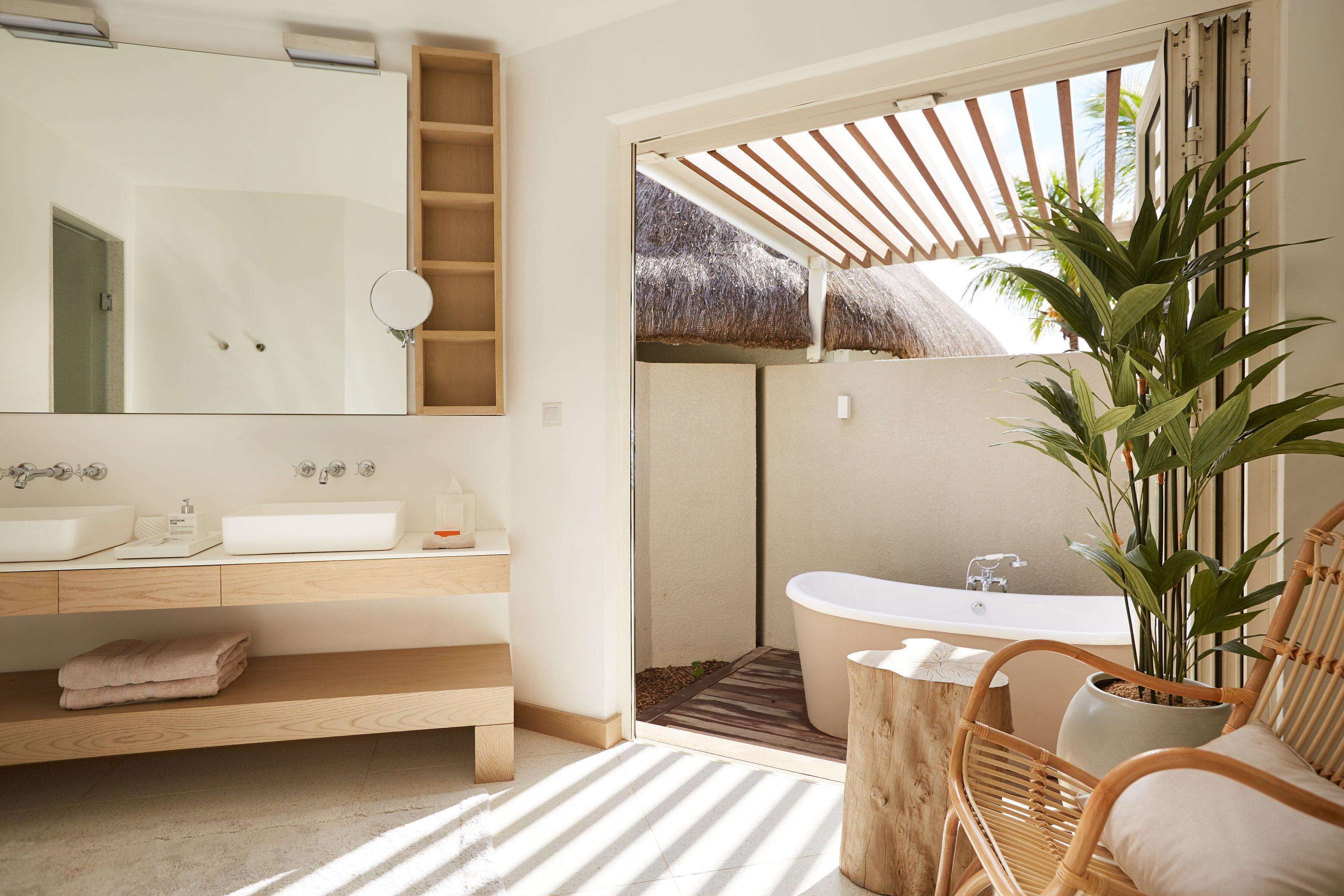 Une salle de bain moderne avec un grand miroir, deux lavabos, une baignoire et une chaise en bois.
