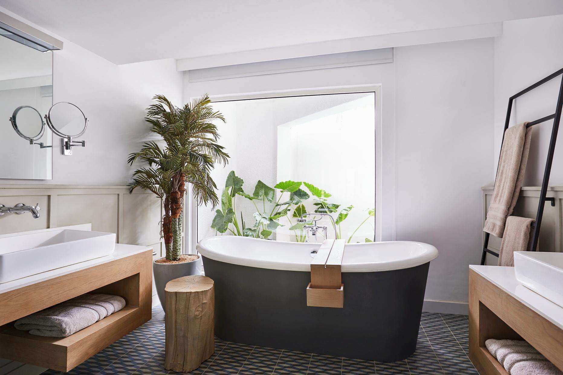 Un baño moderno con una bañera independiente, dos lavamanos, un espejo grande y una planta en maceta.
