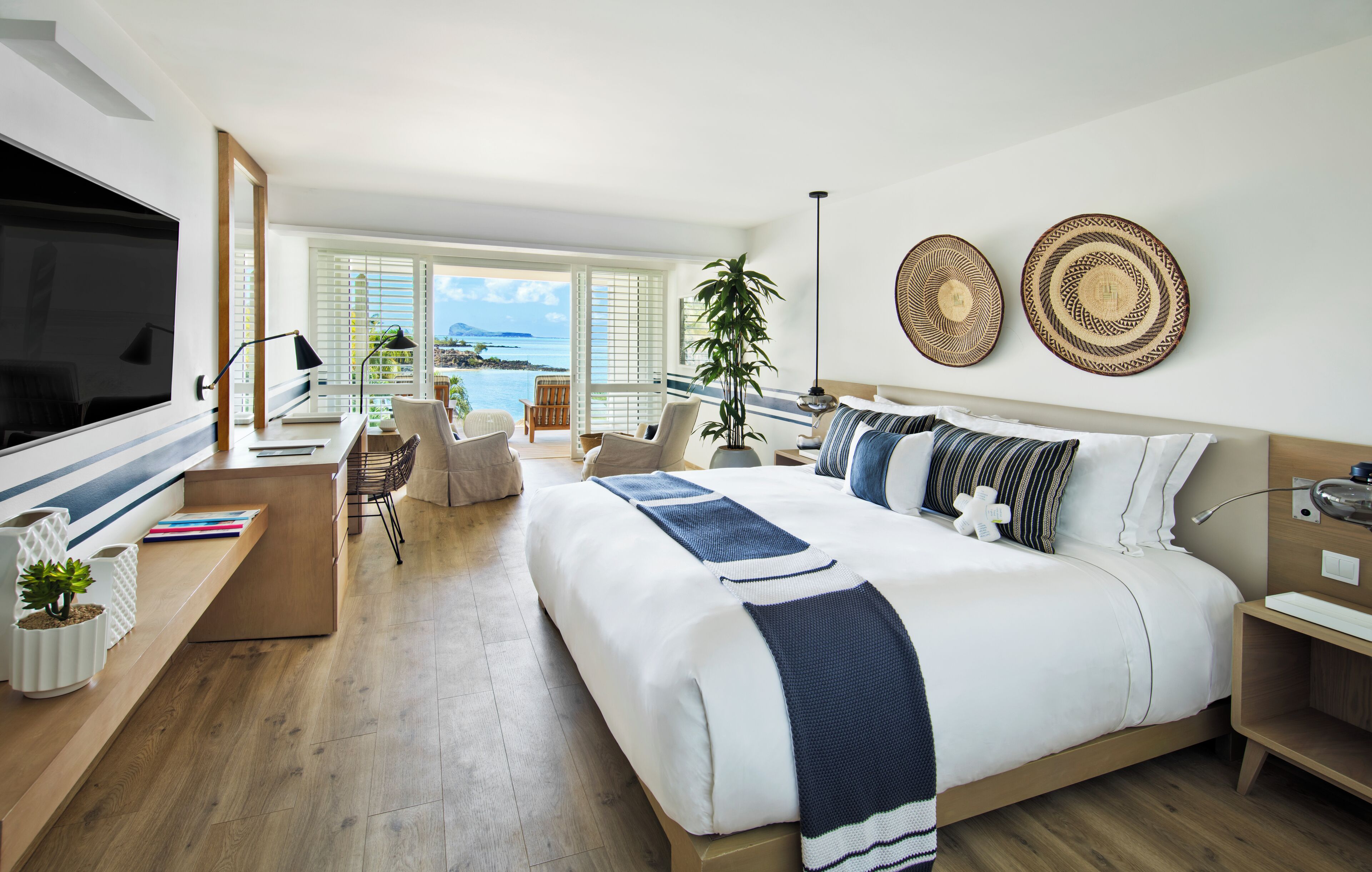 A modern hotel room with a large bed, a desk, and a view of the ocean.